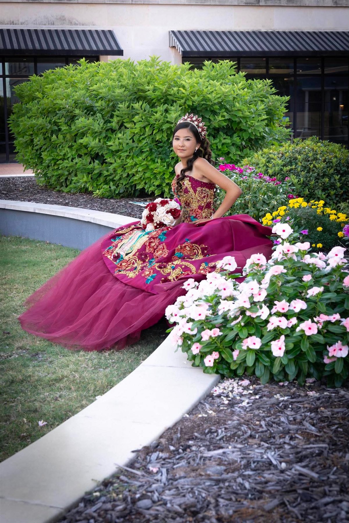 Quinceañera in a burgundy gown in a garden